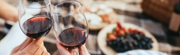 Panoramic crop of couple clinking glasses with red wine — Stock Photo