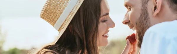 Image horizontale de la femme heureuse en chapeau de paille nourrir l'homme avec fraise mûre — Photo de stock