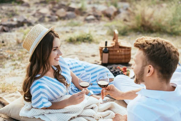 Selective focus of happy woman in straw hat and bearded man holding glasses with red wine — Stock Photo