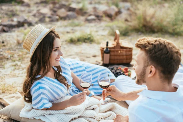 Enfoque selectivo de la mujer feliz en sombrero de paja y hombre barbudo sosteniendo vasos con vino tinto - foto de stock