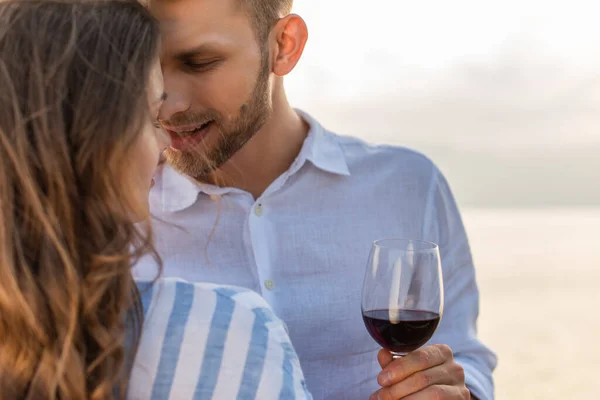 Enfoque selectivo del hombre barbudo mirando a la novia y sosteniendo el vaso con vino tinto - foto de stock