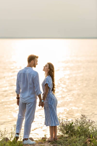 Handsome man and attractive woman holding hands near lake — Stock Photo