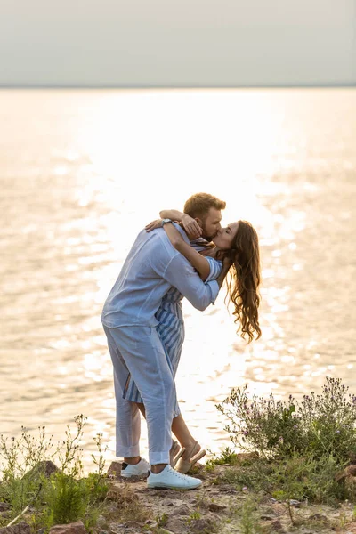 Hombre guapo y atractiva mujer besándose cerca del lago - foto de stock