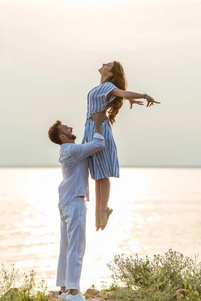 Profile of happy man holding in arms happy woman in dress near lake — Stock Photo