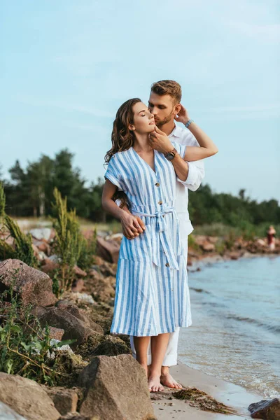 Bärtiger Mann küsst attraktives Mädchen in der Nähe von grünen Pflanzen und See — Stockfoto