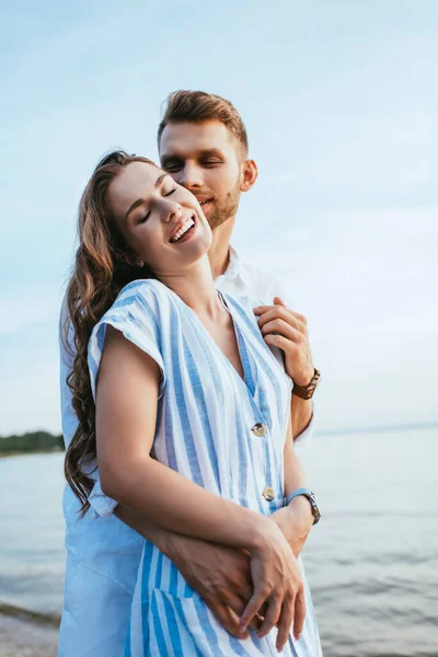 Bearded man smiling and hugging cheerful girl near lake — Stock Photo