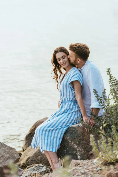 Fuoco selettivo di uomo barbuto baciare ragazza allegra vicino al fiume — Foto stock