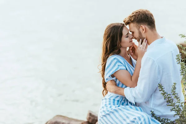 Mujer feliz tocando la cara de novio guapo cerca del río - foto de stock