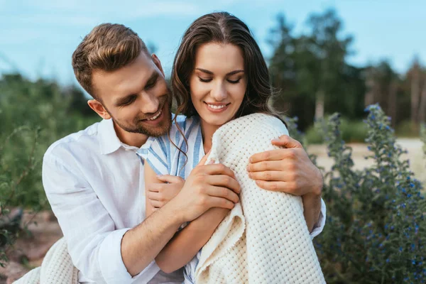 Barbudo hombre sonriendo y tocando manta mientras abrazando novia fuera - foto de stock