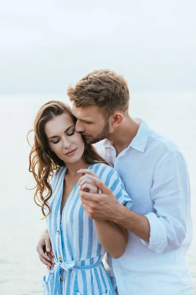 Bearded man kissing and holding hands with attractive girl — Stock Photo