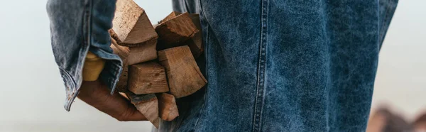 Panoramic crop of man in denim jacket holding firewood — Stock Photo