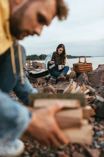 Selektiver Fokus von Mädchen, die Kaffee einschenken, während sie Thermoskannen in der Nähe von Weidenkorb, akustischer Gitarre und Freund halten — Stockfoto