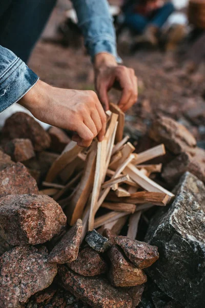 Foco seletivo do homem tocando paus ao fazer fogueira perto de pedras — Fotografia de Stock