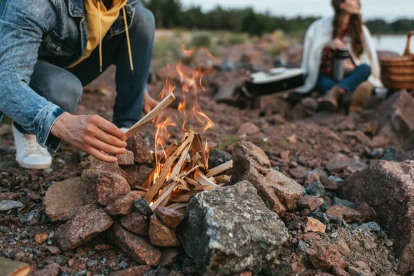 Selective focus of man holding stick while making bonfire near woman — Stock Photo