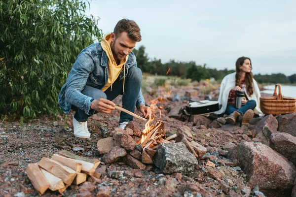 Selective focus of handsome man holding stick near burning bonfire and woman — Stock Photo