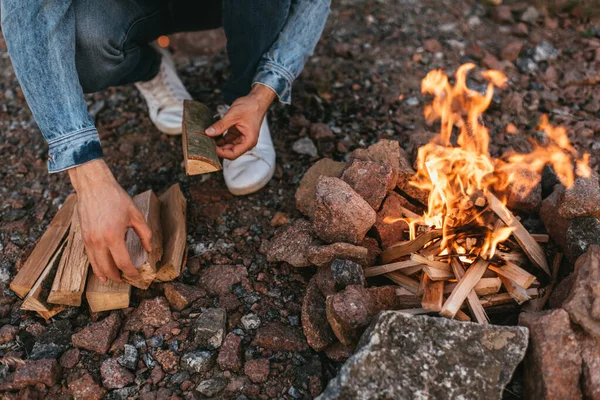 Cropped view of man touching wooden log near burning bonfire — Stock Photo