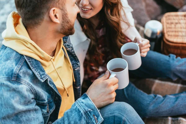 Vista recortada de hombre y mujer feliz sosteniendo tazas con té al aire libre - foto de stock