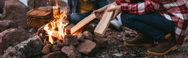 Panoramic crop of woman putting log in burning bonfire — Stock Photo