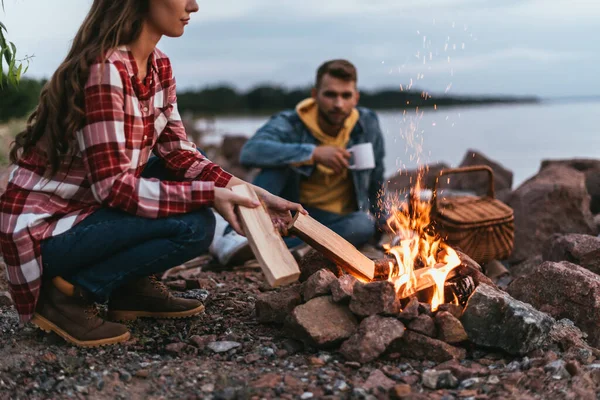 Selective focus of young woman putting log in burning bonfire — Stock Photo
