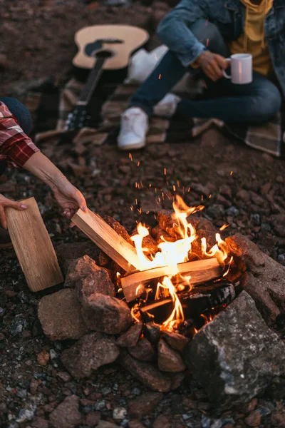Cropped view of woman putting log in burning bonfire — Stock Photo