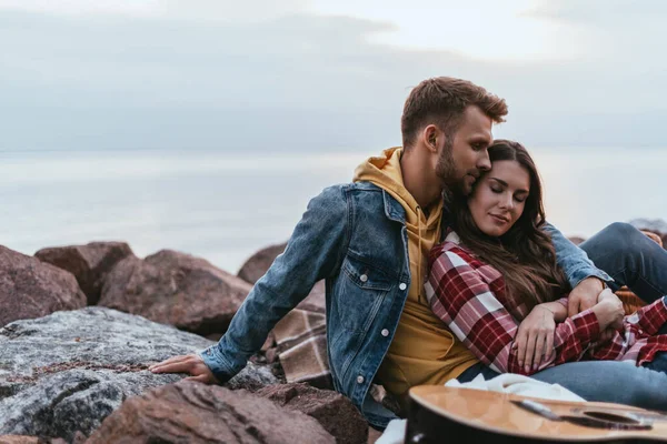 Selective focus of handsome man hugging girlfriend near acoustic guitar — Stock Photo