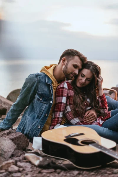 Selektiver Fokus eines glücklichen Paares mit geschlossenen Augen, das neben einer Akustikgitarre sitzt — Stockfoto