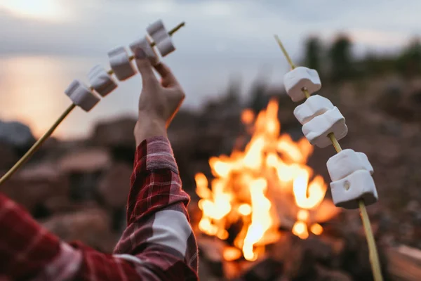 Cropped view of couple holding sticks with puffy marshmallows near bonfire — Stock Photo