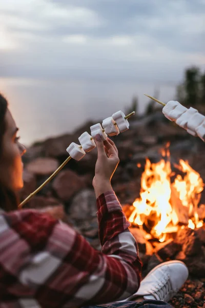 Foco seletivo de menina segurando pau com marshmallows inchado perto de fogueira — Fotografia de Stock