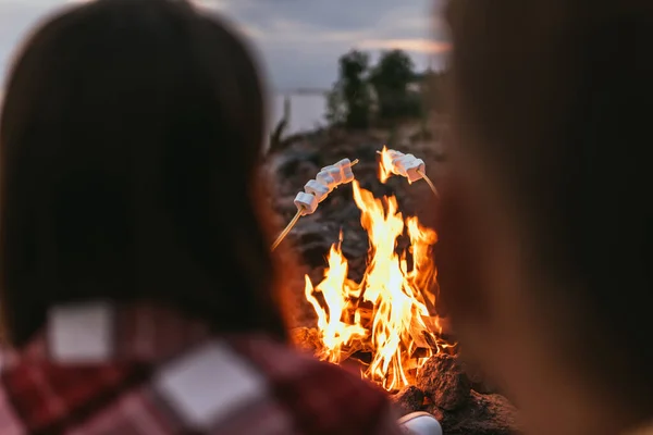 Selektiver Fokus geschwollener Marshmallows auf Stöcke in der Nähe von Lagerfeuer und Paar — Stockfoto