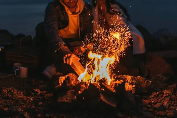 Cropped view of man putting log in bonfire near girl — Stock Photo