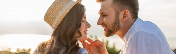 Horizontales Bild eines Mannes, der das Gesicht einer fröhlichen Frau mit Strohhut berührt — Stockfoto