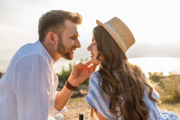Happy man touching face of cheerful woman in straw hat — Stock Photo