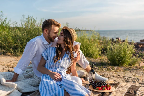 Casal feliz olhando um para o outro enquanto sentado perto de comida saborosa e garrafa com vinho — Fotografia de Stock