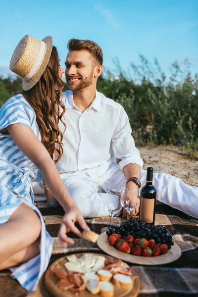 Selective focus of happy couple sitting near tasty food and bottle with wine — Stock Photo