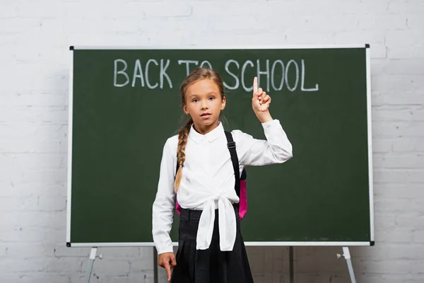 Adorable écolière pointant du doigt à l'inscription de retour à l'école sur tableau noir — Photo de stock