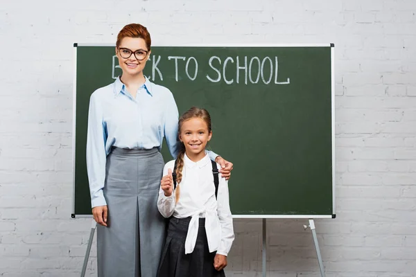 Lächelnder Lehrer berührt Schulter einer glücklichen Schülerin in der Nähe von Kreidetafel mit Schulschriftzug — Stockfoto