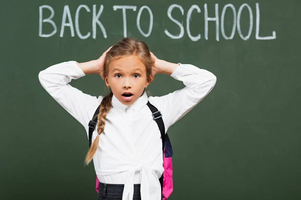 Choqué écolière toucher la tête près de tableau noir avec retour à l'école lettrage — Photo de stock