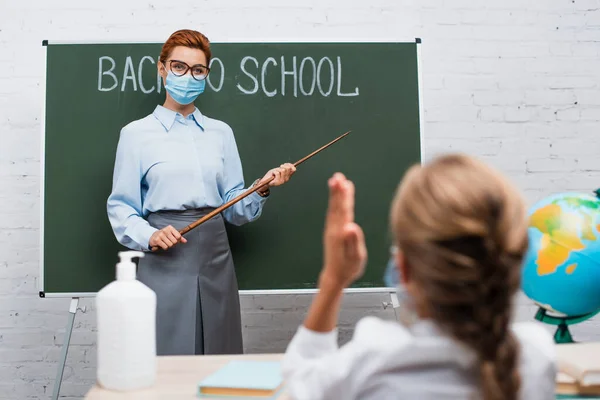 Vista posterior de la colegiala con la mano levantada y el profesor con palo de apuntar cerca de pizarra con letras de vuelta a la escuela - foto de stock