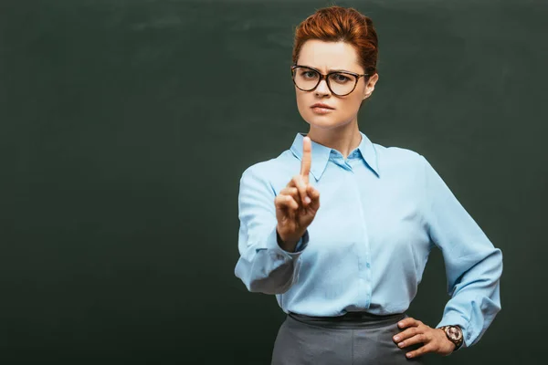Суворий вчитель в окулярах показує стоп- жест, стоячи біля крейдяної дошки — стокове фото