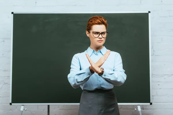 Profesor serio en gafas que muestran gesto de parada mientras está de pie cerca de pizarra - foto de stock