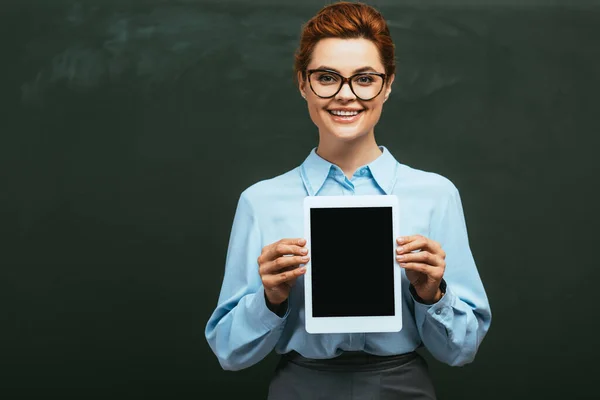 Fröhliche Lehrerin zeigt digitales Tablet mit leerem Bildschirm, während sie neben der Tafel steht — Stockfoto