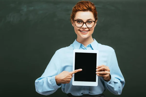 Enseignant heureux pointant avec le doigt à la tablette numérique avec écran blanc près du tableau — Photo de stock