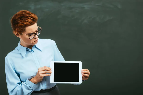 Вдумчивый учитель смотрит на цифровой планшет с чистым экраном рядом с доской — стоковое фото