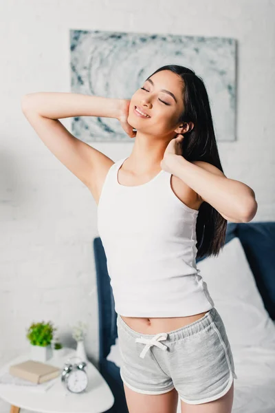 Beautiful asian girl smiling while stretching in bedroom — Stock Photo