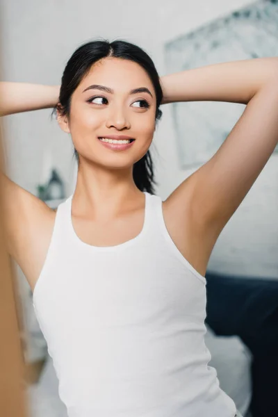 Enfoque selectivo de alegre chica asiática mirando hacia otro lado en dormitorio - foto de stock