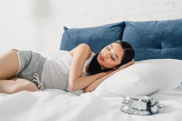 Selektiver Fokus einer Asiatin, die in der Nähe des Weckers auf dem Bett schläft — Stockfoto