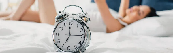 Horizontales Bild des Weckers in der Nähe einer Frau, die morgens auf dem Bett liegt — Stockfoto