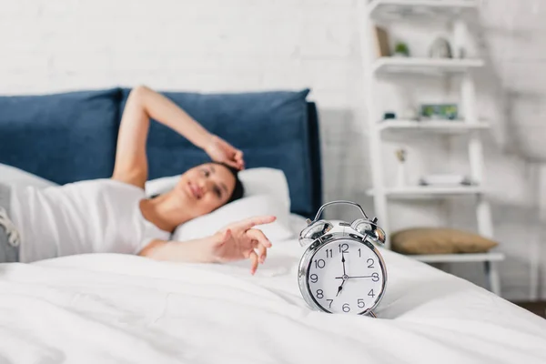 Enfoque selectivo de sonriente mujer asiática tirando de la mano a despertador en la cama por la mañana - foto de stock