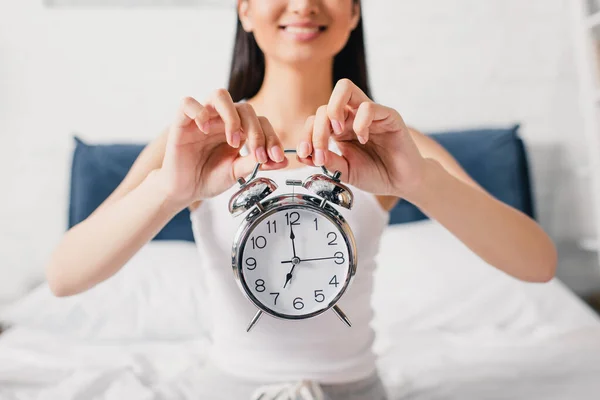 Selective focus of smiling woman holding alarm clock in bedroom at morning — Stock Photo