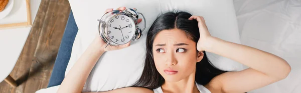 Horizontal crop of sad asian woman holding alarm clock on bed at morning — Stock Photo